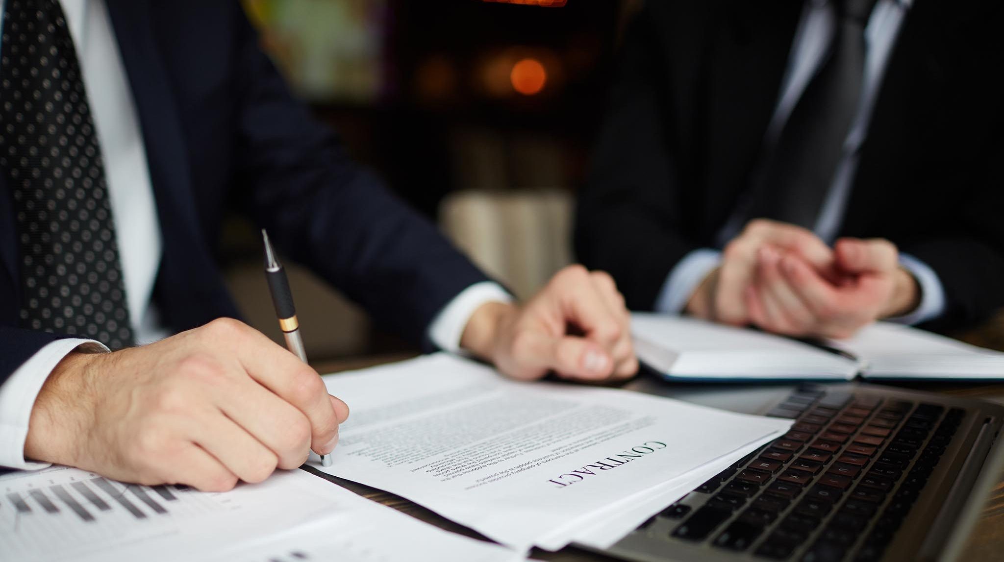 Closeup portrait of unrecognizable successful businessman wearing black formal suit reviewing documents and signing contract during meeting
